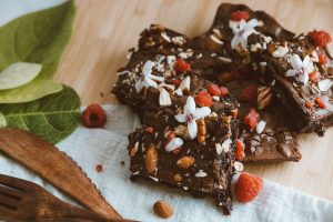 Rich chocolate brownies topped with raspberries, nuts, and flowers on a wooden table.